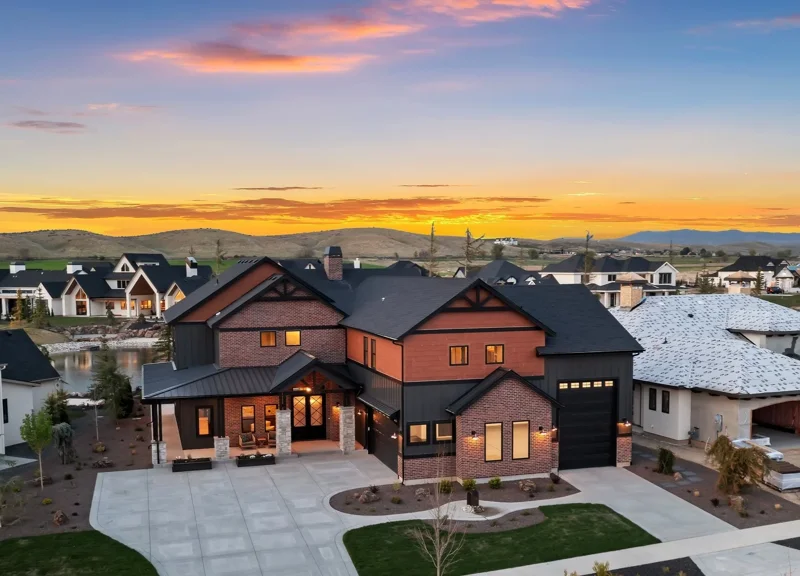 Aerial view of the Bowers in Terra View. A modern two-story house with a black and brick exterior, large driveway, and front porch, located in Terra View during sunset with a colorful sky and neighboring houses nearby. 2025 Spring Parade Home.